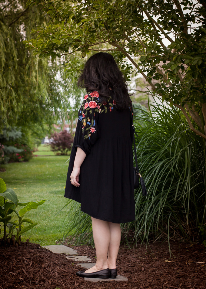 Back of the black floral embroidered dress worn while standing in the garden.